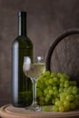 A bottle of white wine, a glass of white wine on a background of grapes and barrel on wooden table Royalty Free Stock Photo