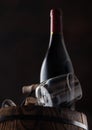 Bottle of wine and empty classic wine glass with corks and vintage corkscrew on top of wooden barrel on black