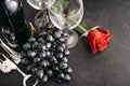 Bottle of wine, 2 empty glasses, bunch of dark grapes, red rose flower, corkscrew on a black background, top view Royalty Free Stock Photo