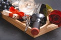 Bottle of wine, 2 glasses, 1 red rose, gift box with ribbon, dark grapes, corkscrew on black Royalty Free Stock Photo