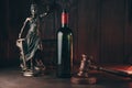 Bottle of wine and lady of justice and judge gavel as a symbol of law on a wooden table