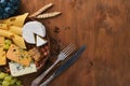 A bottle of wine, and a large assortment of cheeses, honey, nuts and spices, on a wooden table. Top view.