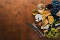 A bottle of wine, and a large assortment of cheeses, honey, nuts and spices, on a wooden table. Top view.