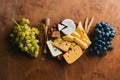 A bottle of wine, and a large assortment of cheeses, honey, nuts and spices, on a wooden table. Top view.