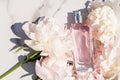 A bottle of women`s perfume with a floral fragrance among the delicate peony on a marble background. the concept of perfumery and Royalty Free Stock Photo