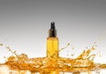 The bottle of the yellow cosmetic in the big oil splash on the gradient grey background