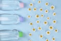 Bottles with baby oil and daisies on light blue background, flat lay