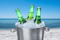 Bottles of beer with ice cubes in metal bucket against blurred sea and beach Royalty Free Stock Photo