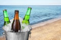 Bottles of beer with ice cubes in metal bucket against blurred sea and beach. Space for text Royalty Free Stock Photo