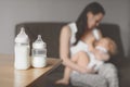 Bottles with breast milk on the background of mother holding in her hands and breastfeeding baby. Maternity and baby care.