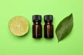 Bottles of citrus essential oil, fresh lime and leaf on green background, flat lay Royalty Free Stock Photo