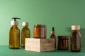 Bottles for cosmetics and cream on a pedestal, green background. Brown glass jars with wooden lids. Eco concept.