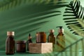 Bottles for cosmetics and cream on a pedestal, green background with leaves and shadow. Brown glass jars with wooden