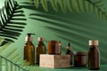 Bottles for cosmetics and cream on a pedestal, green background with leaves and shadow. Brown glass jars with wooden