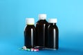 Bottles of cough syrup, dosing spoon and pills on light blue background Royalty Free Stock Photo