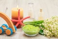 Bottles with cream for face skin and aromatic oil, bowl with sea salt, burning candle, starfish, hand massager and bouquet of