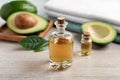 Bottles of essential oil, fresh avocado and towels on light wooden table Royalty Free Stock Photo