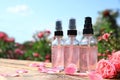 Bottles of facial toner with essential oil and fresh roses on wooden table against blurred background Royalty Free Stock Photo