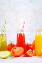 Bottles with fresh orange, apple, tomato juice and colored tubules on a gray concrete table. Royalty Free Stock Photo