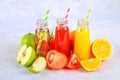 Bottles with fresh orange, apple, tomato juice and colored tubules on a gray concrete table. Royalty Free Stock Photo