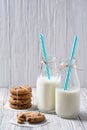 Two bottles of milk with straws and chocolate chip cookies on wooden background Royalty Free Stock Photo