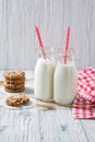 Bottles of milk with red striped straws and chocolate chip cookies on wooden background Royalty Free Stock Photo