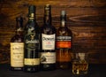 4 bottles of premium 12 year old Scotch whisky: Balvenie, Auchentoshan, Glenfiddich, Dewars and a glass of ice on a dark