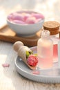 Bottles of rose essential oil and flowers on white wooden table, closeup Royalty Free Stock Photo