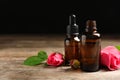 Bottles of rose essential oil and flowers on wooden table against black background Royalty Free Stock Photo