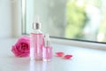 Bottles of rose essential oil and fresh flower on window sill