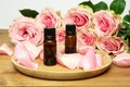 Bottles of rose essential oil with rose petals on the background of beautiful pink roses on wooden table