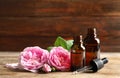Bottles of rose essential oil, pipette and flowers on wooden table Royalty Free Stock Photo