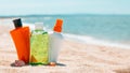 Bottles of sun protection lotion, aloe soothing gel from sun burn, seashells in sand on the beach with sparkling sea in Royalty Free Stock Photo