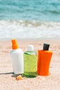 Bottles of sun protection lotion, aloe soothing gel from sun burn, seashells in sand on the beach with sparkling sea in Royalty Free Stock Photo