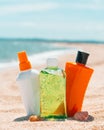 Bottles of sun protection lotion, aloe soothing gel from sun burn, seashells in sand on the beach with sparkling sea in Royalty Free Stock Photo