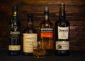 Bottles of 12 year old Balvenie, Auchentoshan, Glenfiddich, Dewars whiskey and a glass with ice on a dark wooden