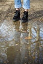 Bottom half of a person`s legs wearing boots and standing in front of a puddle of mud in a forest with the person and the trees Royalty Free Stock Photo
