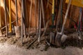 The bottom half of a selection of gardening tools including spade, fork, sledge hammer and rake inside a dusty shed Royalty Free Stock Photo