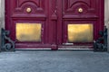 Bottom side of dark red painted wooden door protected with shiny golden metal plates and black metal ornate elements by corners.