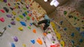 BOTTOM UP: Teenage climber climbs up an indoor wall filled with colorful holds.