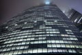 A bottom-up view of the facade of a modern office building at night in fog. Light of the night city. Moscow City Royalty Free Stock Photo