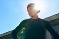 Bottom view of an athlete in sportswear with hands on the waist posing on a sunlight. Portrait of an athletic man taking a break