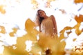 Bottom view of beautiful playful woman surrounded by yellow leaves on background of autumn forest and sky Royalty Free Stock Photo