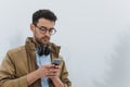 Bottom view of Caucasian man walking outdoor in foggy weather, messaging via social networks at smart phone and using headphones Royalty Free Stock Photo