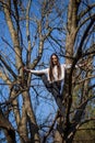 Bottom view charming cute slim girl is on top of unusual tree without leaves on background sky