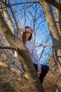 Bottom view charming cute slim girl is on top of unusual tree without leaves on background sky