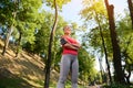 Bottom view of a confident 30 years old pretty woman in sportswear standing in a forest city park with her arms crossed and Royalty Free Stock Photo