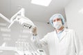 Bottom view of a doctor portrait dentist, surgeon in uniform and mask on his face, wearing glasses, holding lamp in her