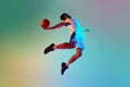 Bottom view dynamic image of young man, basketball player in motion, throwing ball against gradient background in neon