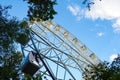 Bottom view of ferris wheel through green tree on background of blue sky Royalty Free Stock Photo